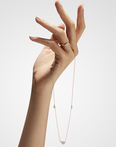 Main de femme portant une bague Birks P&eacute;tale en or jaune et diamants et un collier stationnaire en or jaune et diamants.